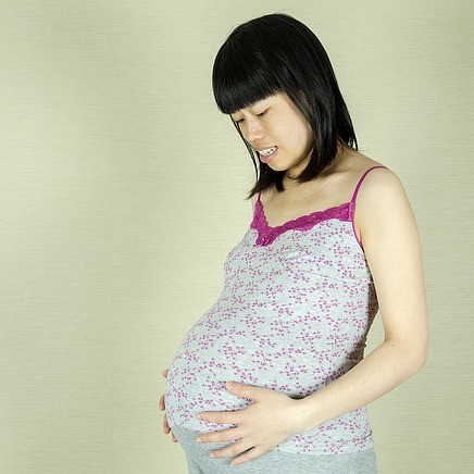 A pregnant woman smiles as she looks down at her belly. A pregnant woman smiles as she looks down at her belly.